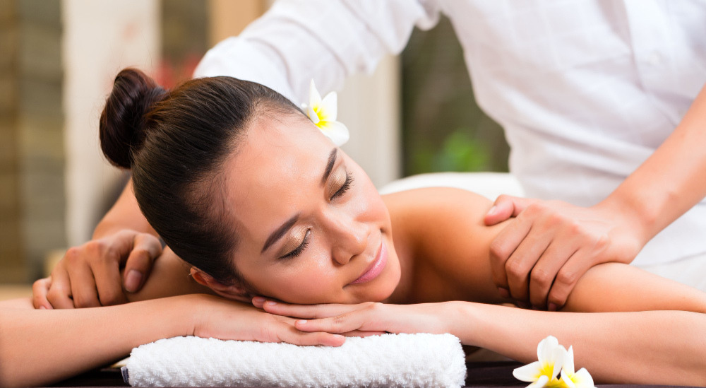 O femeie asiatică din Indonezia, într-un centru spa de wellness și înfrumusețare, beneficiind de un masaj de aromaterapie cu uleiuri esențiale, cu o expresie relaxată